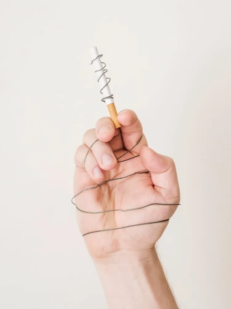 Une main tenant une cigarette montée sur un ressort, les doigts entravés par un fil