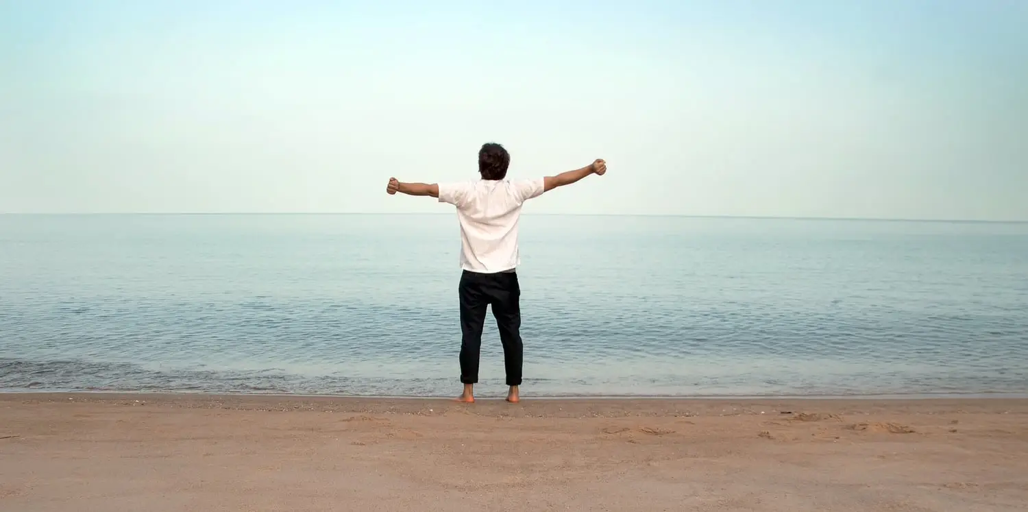 Un homme sur la plage, les bras ouverts face à la mer
